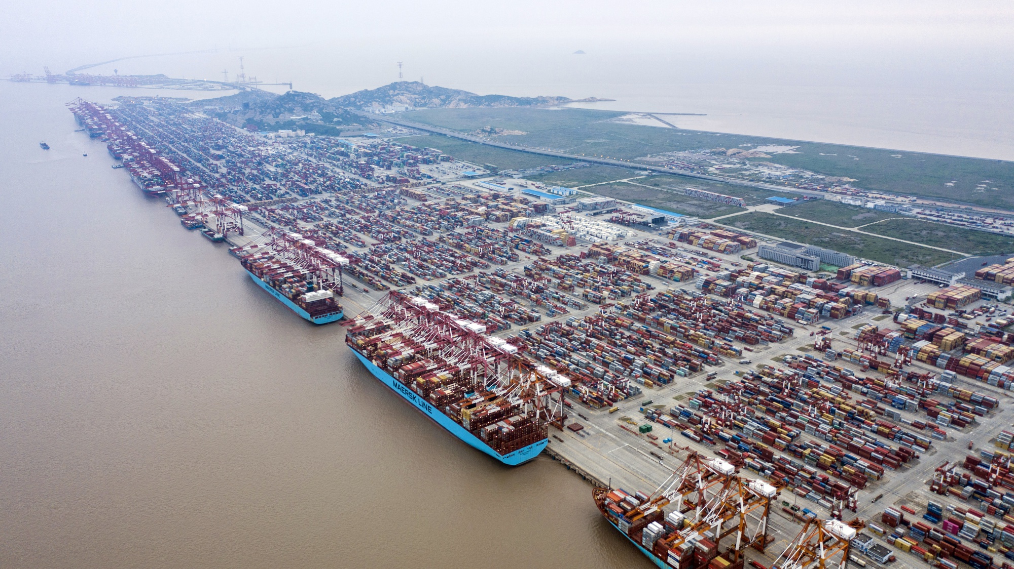 Container ships are docked next to gantry cranes as shipping containers sit stacked at the Yangshan Deepwater Port, operated by Shanghai International Port Group Co. (SIPG), in this aerial photograph taken in Shanghai. Photographer: Qilai Shen/Bloomberg