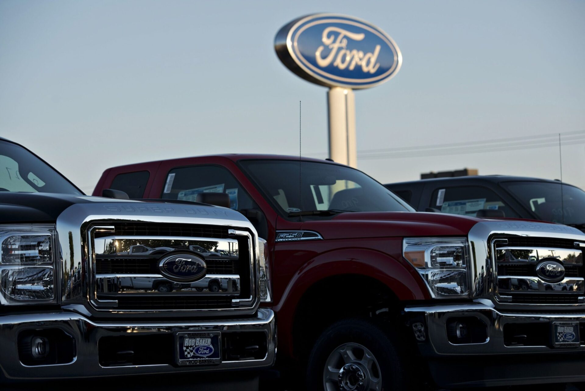 A Ford Motor Co. logo stands behind a row of F-250 pickup trucks at the Rob Baker Ford dealership in Plainfield, Illinois, U.S., on Wednesday, July 23, 2014.