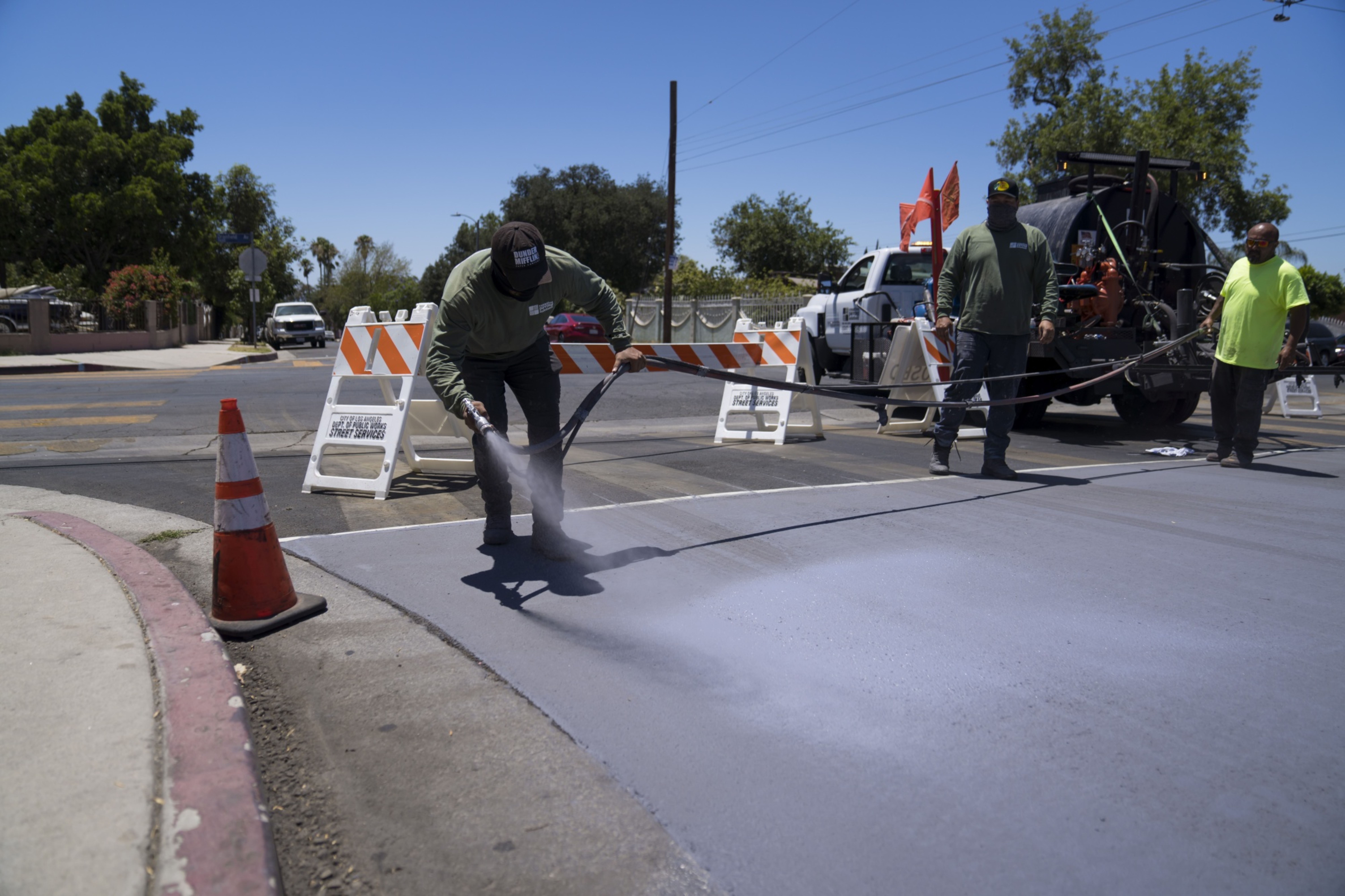 A worker applies a reflective pavement coating to a street in Pacoima, California, US, on Tuesday, July 19, 2022. Reflective coating for parks and pavement can reduce temperatures in lower-income areas with limited shade as climate-driven heat waves become more frequent and intense in Southern California.