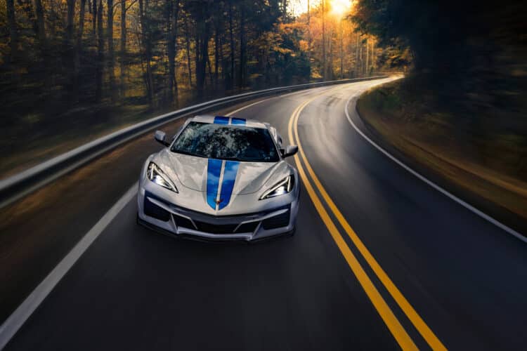 Front view of 2024 Chevrolet Corvette E-Ray 3LZ convertible in Silver Flare with Electric Blue stripe package driving on a road between trees. Pre-production model shown. Actual production model may vary. Model year 2024 Corvette E-Ray available 2023.