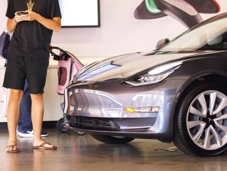 A customer stands next to a Tesla Inc. Model 3 electric vehicle on display at the company's showroom in Newport Beach, California