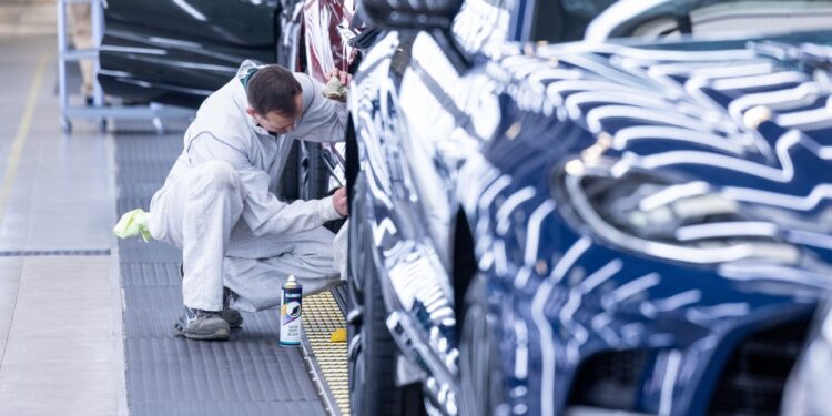 An employee works on a wheel arch of an Aston Martin sport utility vehicle.