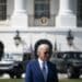 President Biden standing with the White House far behind him, as well as vehicles parked behind him