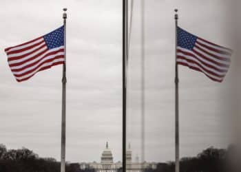 The American flag reflected on building walls in front of the U.S. Capitol building. Photographer: Samuel Corum/Bloomberg