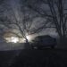 Silhouette of car and trees at night forest with fog, surreal lights mystical landscape