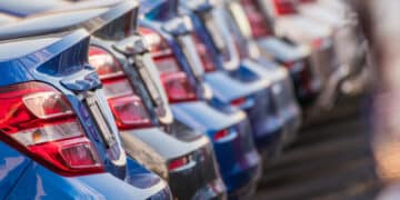 Selection of new metallic blue and gray cars lined up in dealership parking lot.