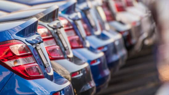 Selection of new metallic blue and gray cars lined up in dealership parking lot.
