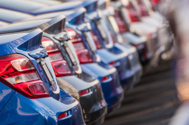Selection of new metallic blue and gray cars lined up in dealership parking lot.