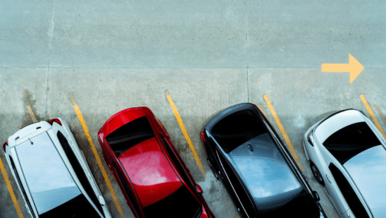 cars lined up in lot with street arrow behind