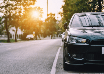 Photo of a parked car framed to show the sun through the trees behind it