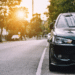 Photo of a parked car framed to show the sun through the trees behind it